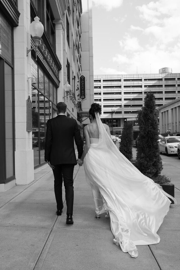 Bride and groom walking down Detroit sidewalk from behind