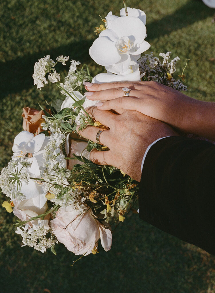 Film shot of bride and groom's ring hands resting on the bridal bouquet