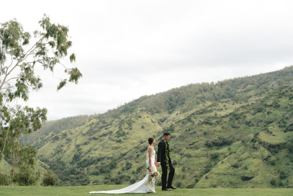 Wide view of bride and groom walking in front of valley in North Shore Oahu