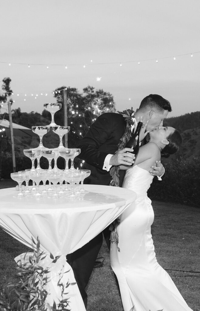 Groom dipping bride for a kiss beside champagne tower