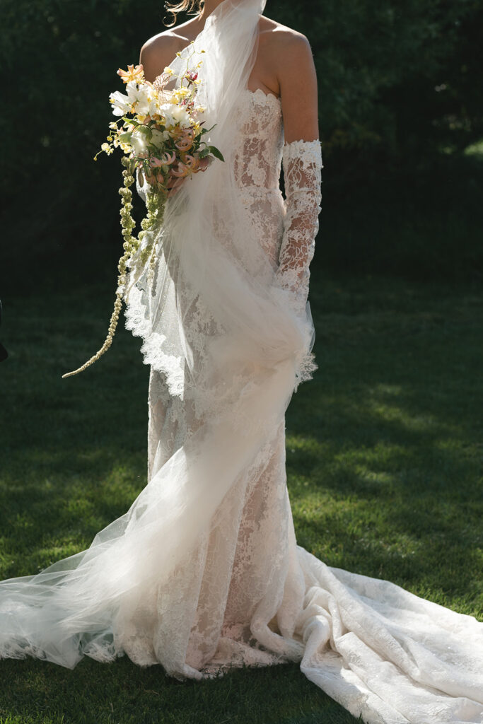 Bride with lace gown, bridal bouquet, and long veil in the wind