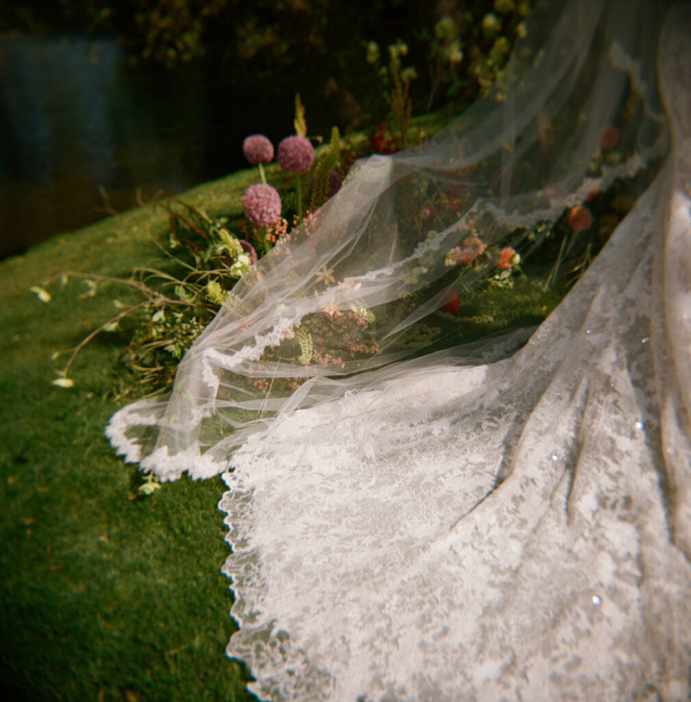 Lace bridal gown train and lace trimmed veil draped over ceremony florals