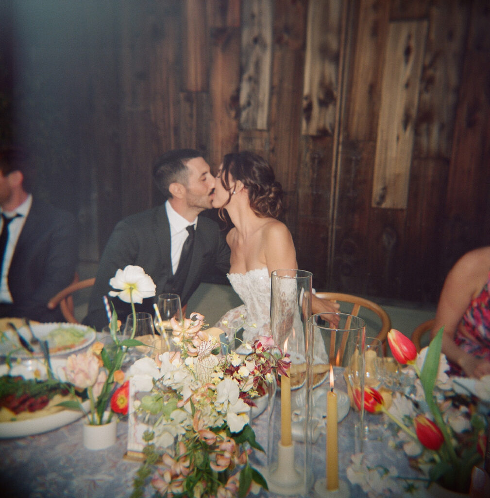 Bride and groom share a kiss in at wedding reception table