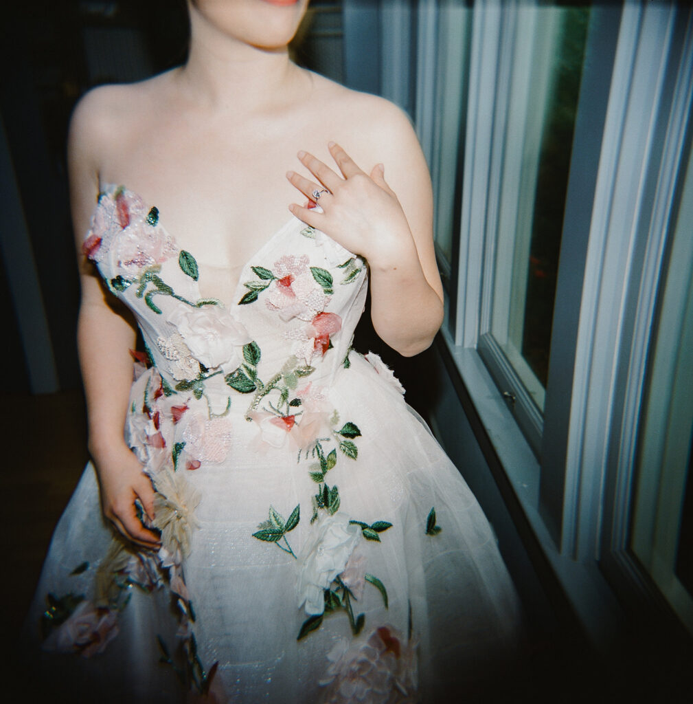 Film portrait of bride in floral gown posing beside window