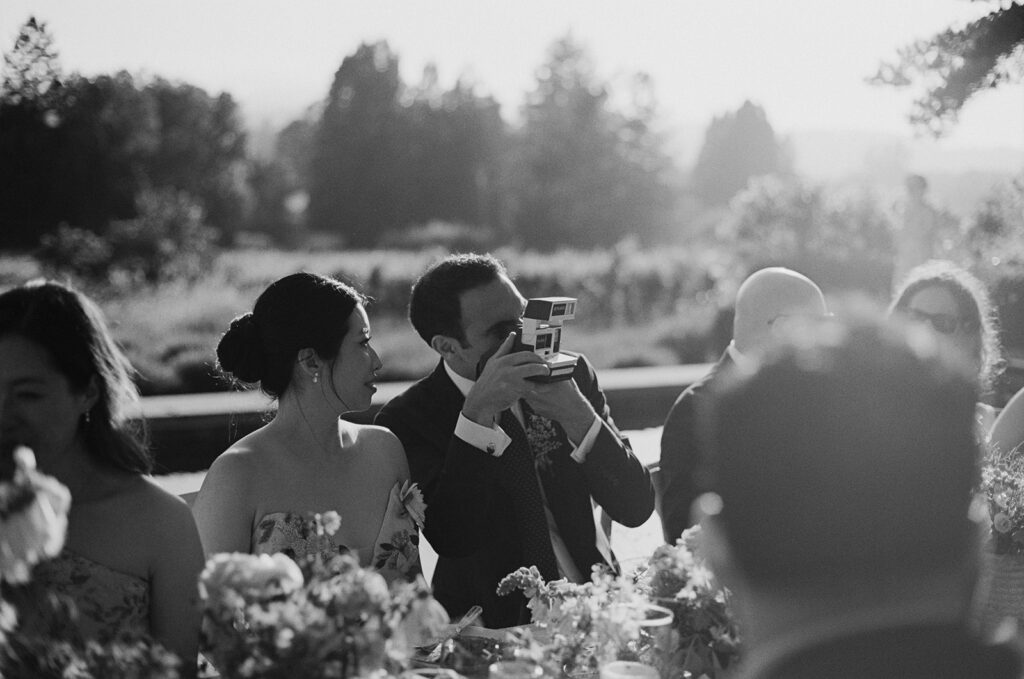 Groom at reception table taking photo with polaroid camera